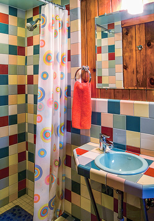 Bathroom with multi colored square tiles, shower and aqua sink.