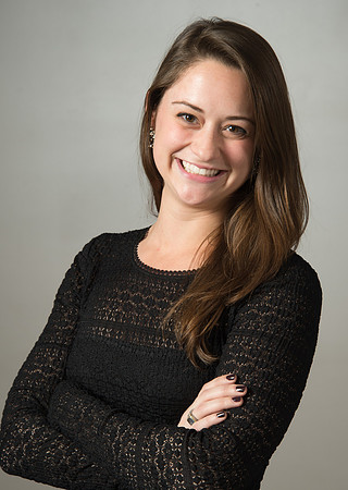 Portrait of smiling young woman wearing black and crossing her arms against grey background