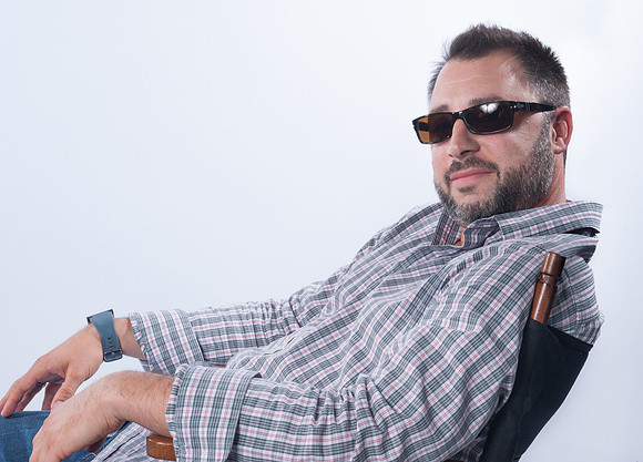 Portrait of young man reclining in chair wearing sunglasses on white background