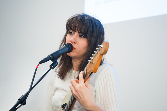 Performer Leah Siegel playing guitar and singing into microphone.