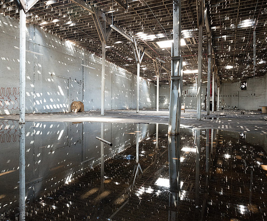 Interior of abandoned warehouse with many holes in roof reflecting off water on floor