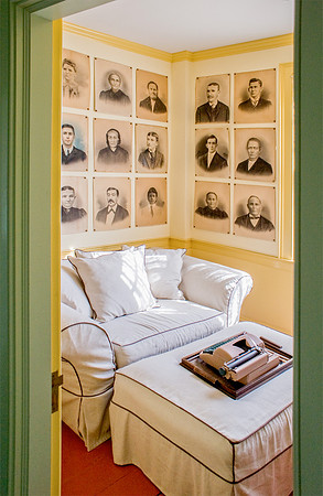 Small yellow room with easy chair and ottoman, old photo portraits on wall arranged in a grid.
