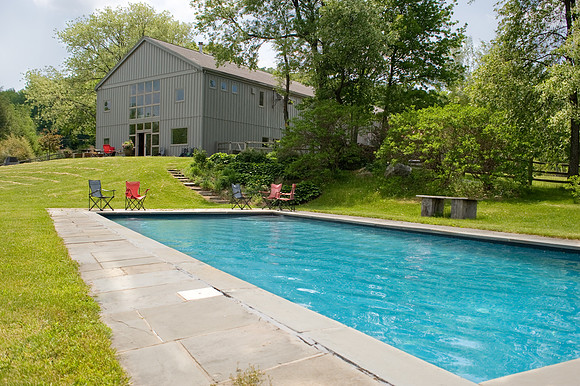 Outdoor swimming pool with trees and home in background.